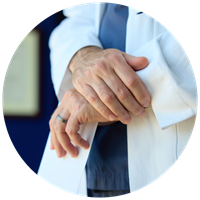 Close-up of a doctor wearing a white coat over scrubs with crossed hands.